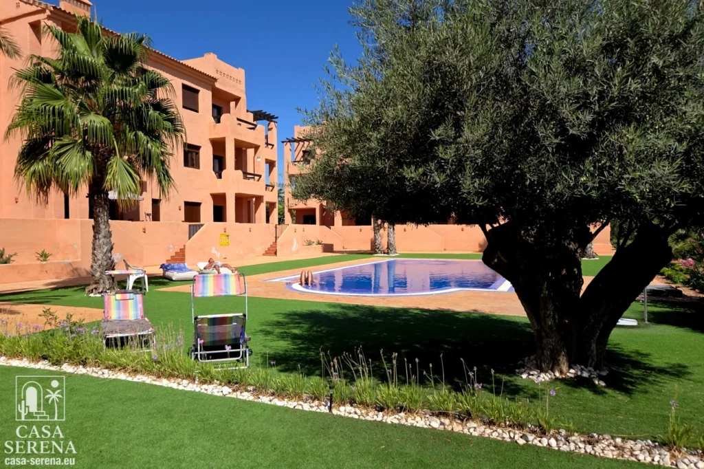 Swimming pool surrounded by lush Mediterranean gardens and palm trees at Casa Serena holiday apartment in Serena Golf, Los Alcázares, Spain.